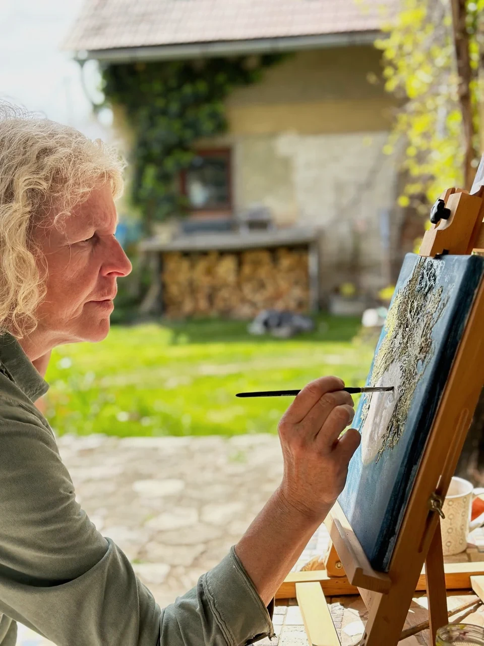 Šimona Vepřková arbeitet im Freien mit einem feinen Pinsel an einer Bildfläche.